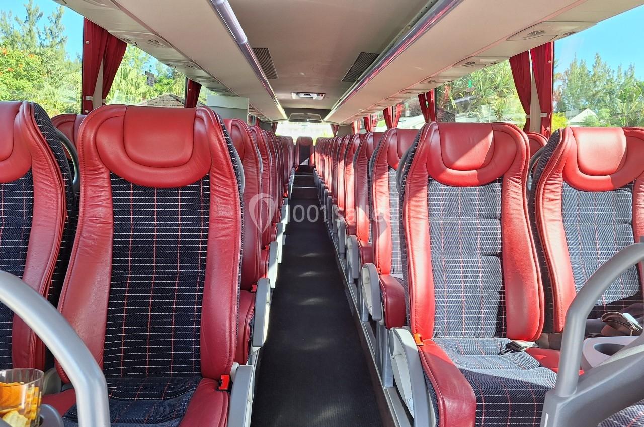 Intérieur d'un autocar avec des sièges rouges et noirs alignés de part et d'autre d'une allée centrale.