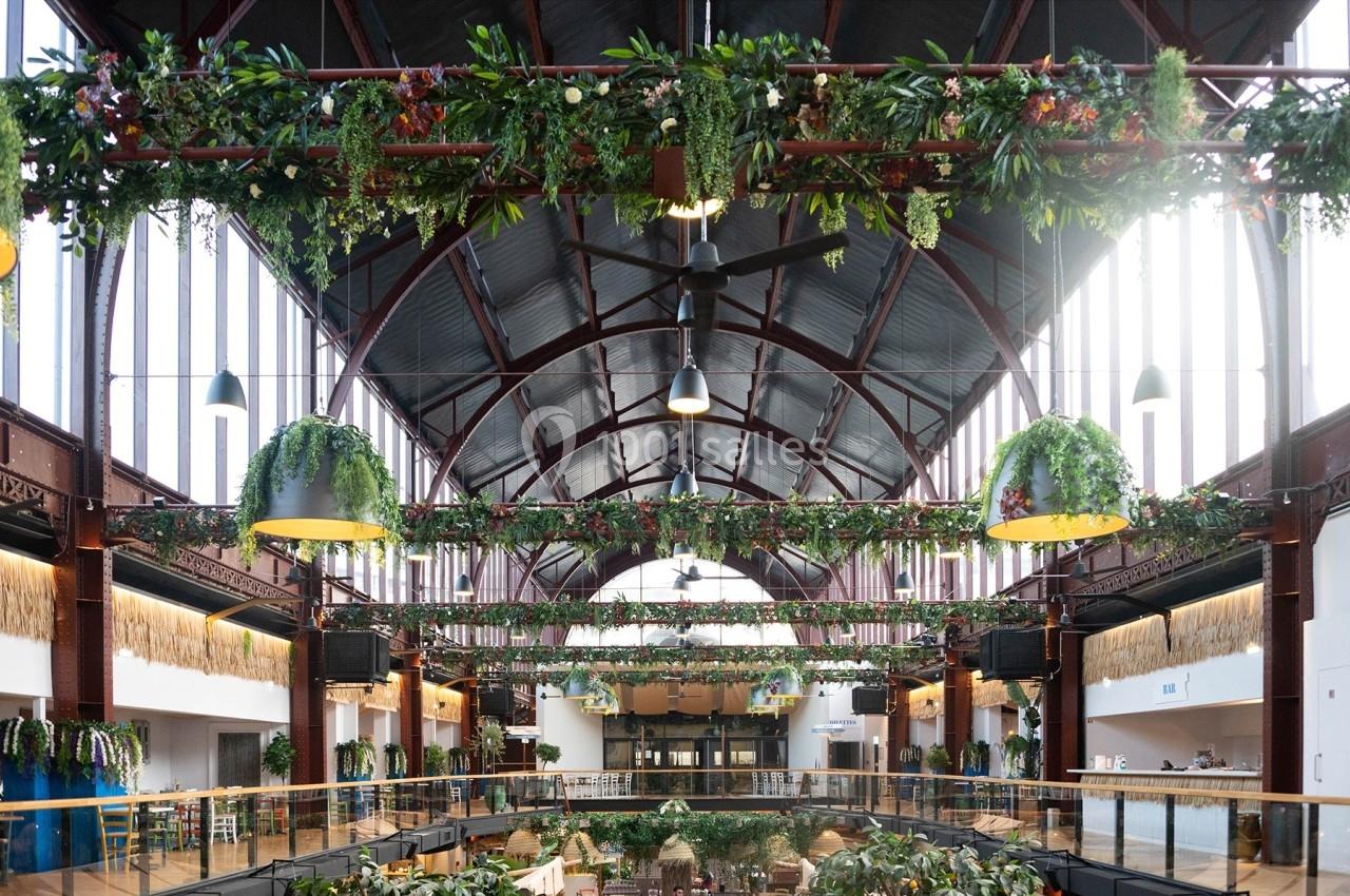 Intérieur d'un marché couvert avec une structure métallique, des plantes suspendues et des espaces lumineux.