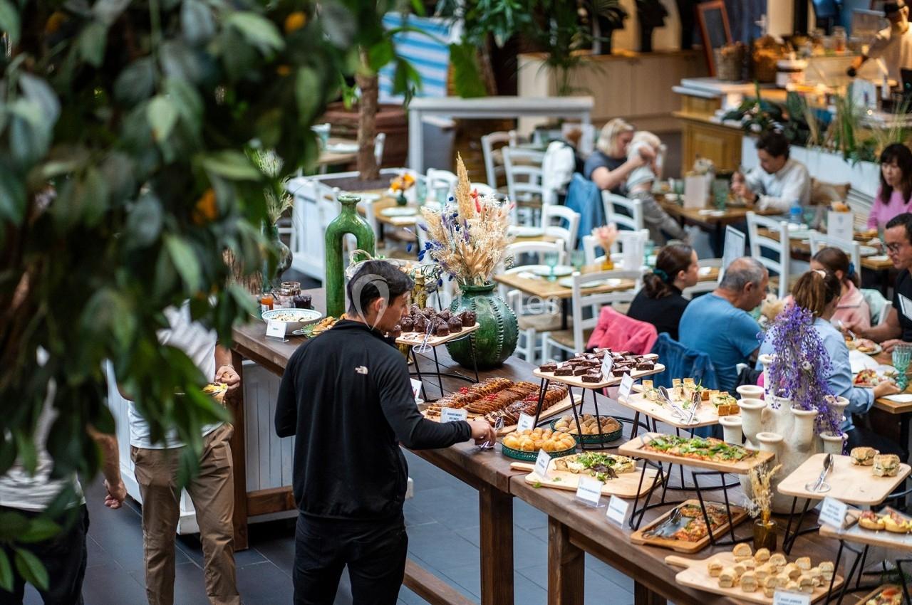 Un homme choisit des plats sur un buffet varié dans un restaurant lumineux avec des tables occupées en arrière-plan.