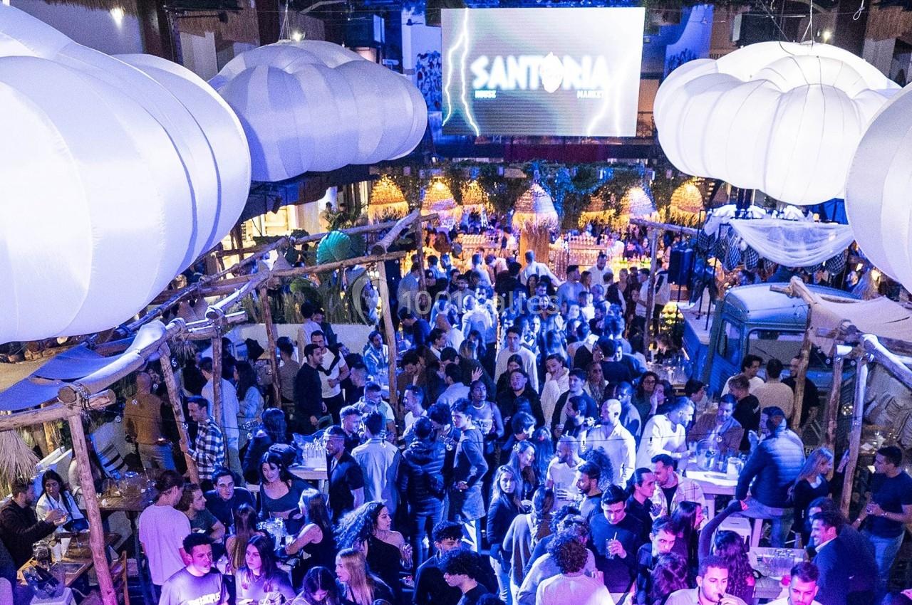 Foule rassemblée dans un lieu festif éclairé par des lumières colorées et décoré de structures suspendues.