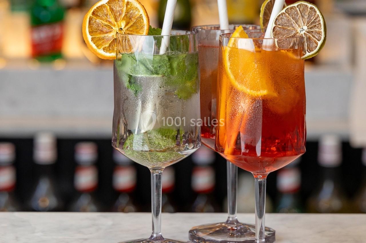 Trois verres de cocktails garnis de tranches d'agrumes et de glaçons, posés sur un comptoir de bar.