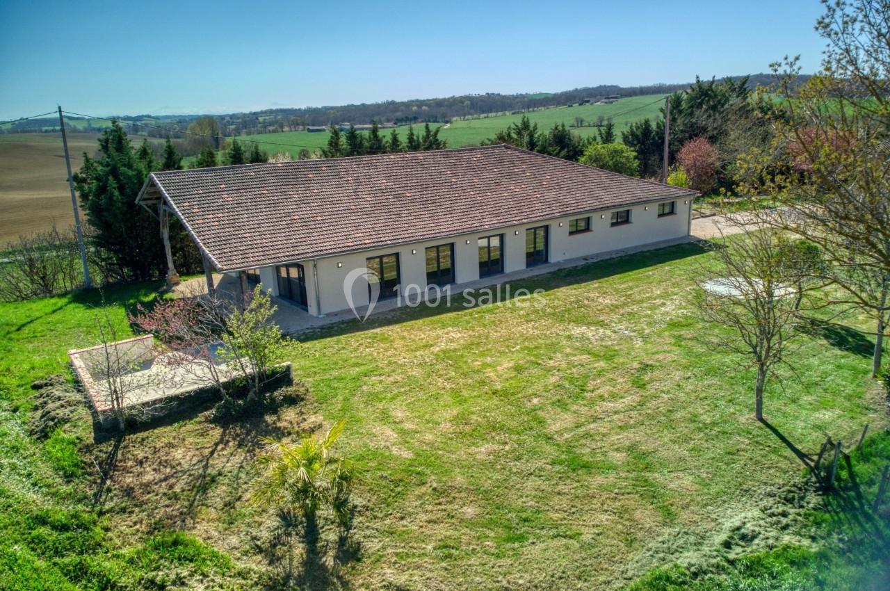 Bâtiment de plain-pied avec toit en tuiles, entouré de pelouse et d'arbres, situé dans un paysage rural.