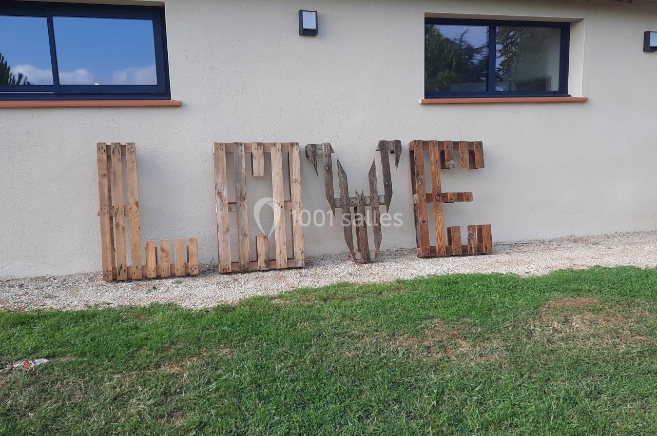 Lettres en bois formant le mot ’LOVE’ posées sur le sol devant un mur clair avec des fenêtres.
