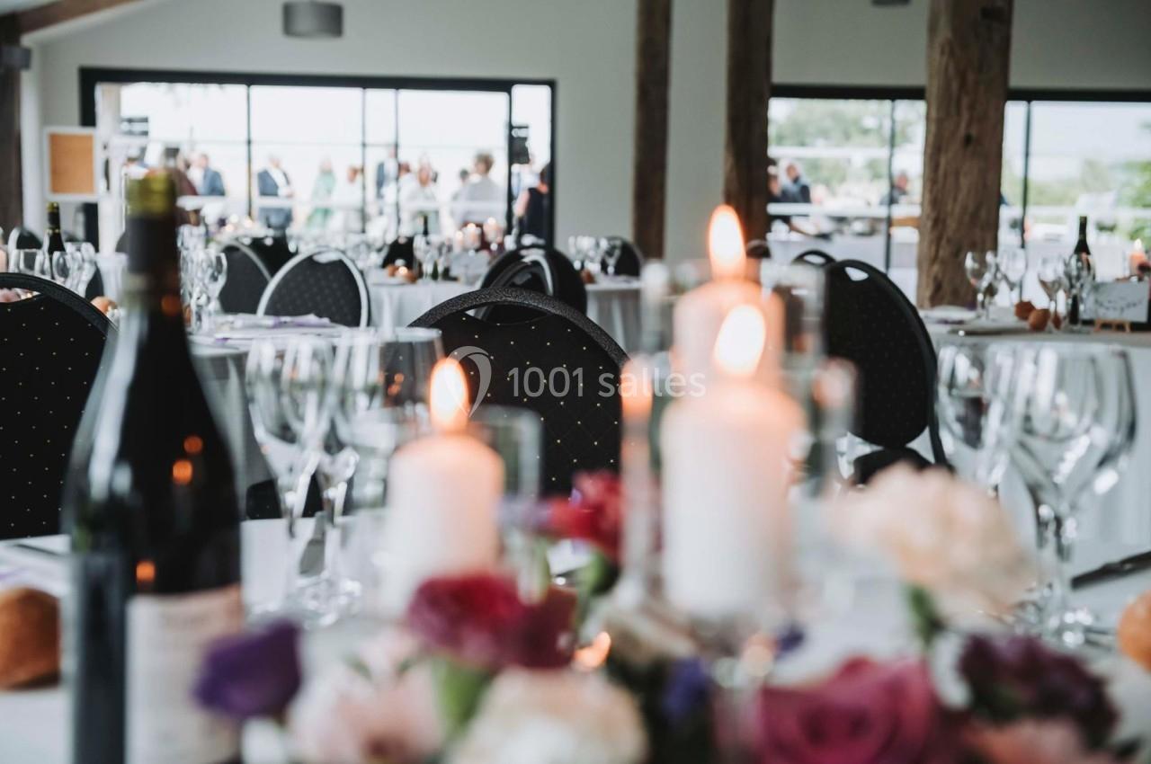 Salle de réception décorée avec des bougies, des fleurs et des tables dressées, vue sur des invités en arrière-plan.