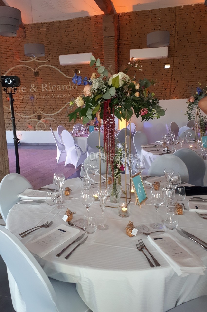 Centre de table floral avec des roses et feuillages sur une table de réception élégamment dressée dans une salle en briques.