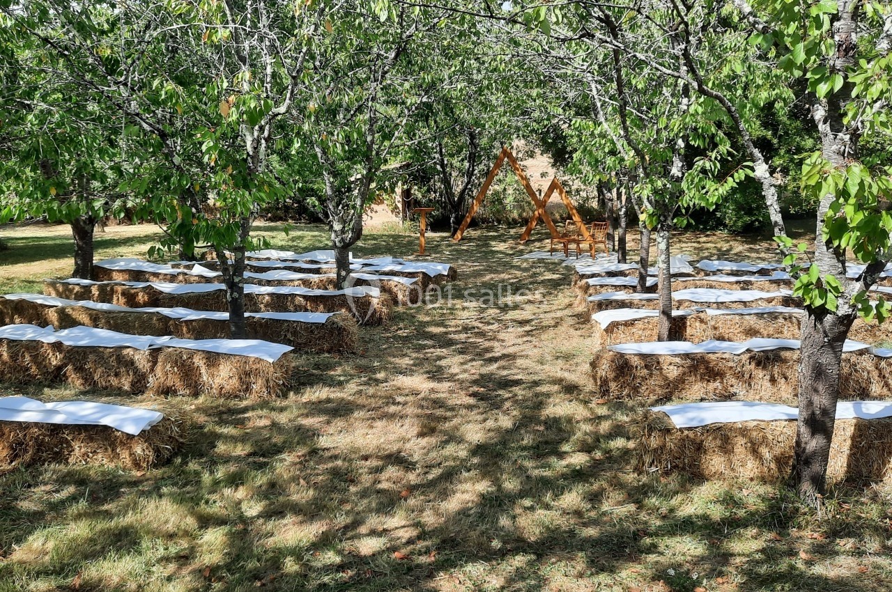Bottes de paille recouvertes de tissu blanc disposées en rangées sous des arbres pour un événement en plein air.