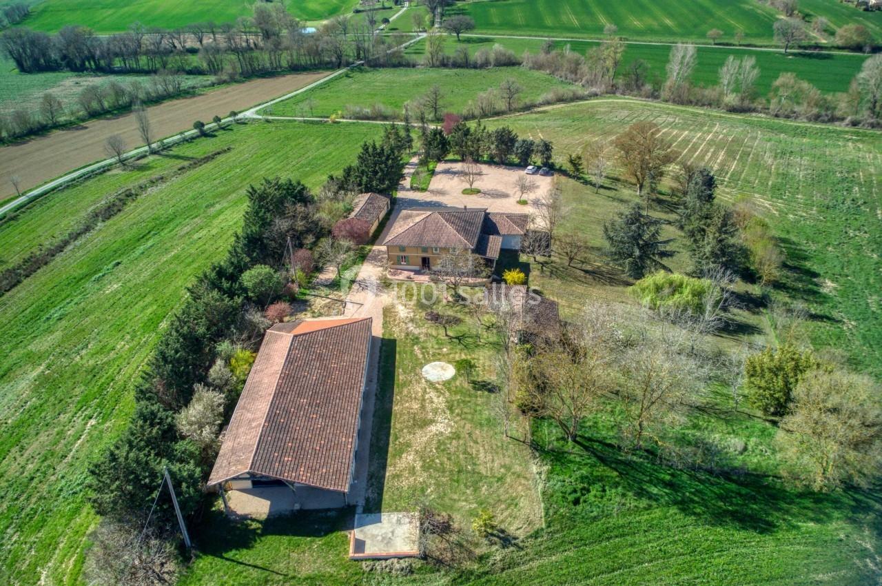 Vue aérienne d'une propriété rurale avec plusieurs bâtiments entourés de champs et d'arbres.