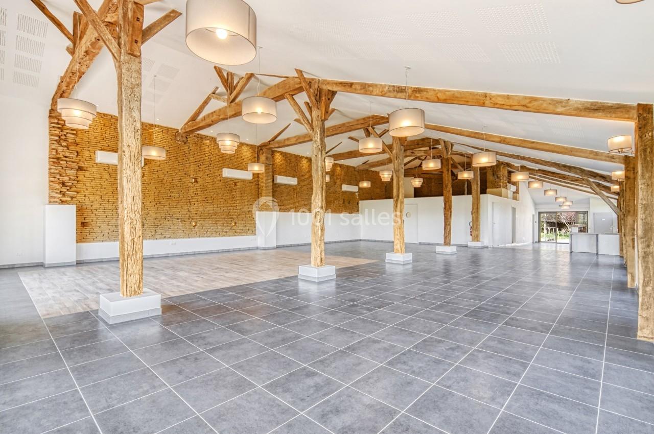 Salle spacieuse avec poutres en bois apparentes, murs en pierre et carrelage gris, éclairée par des suspensions modernes.