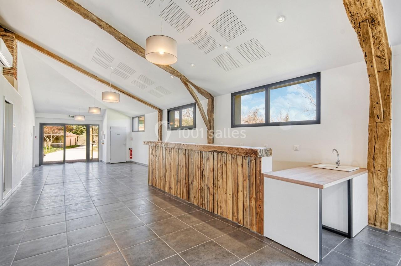 Intérieur lumineux avec comptoir en bois, plafond incliné, poutres apparentes et grandes fenêtres donnant sur l'extérieur.