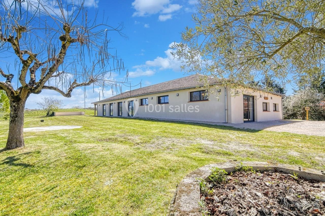 Maison de plain-pied entourée d'un grand jardin avec arbres, sous un ciel bleu parsemé de nuages.