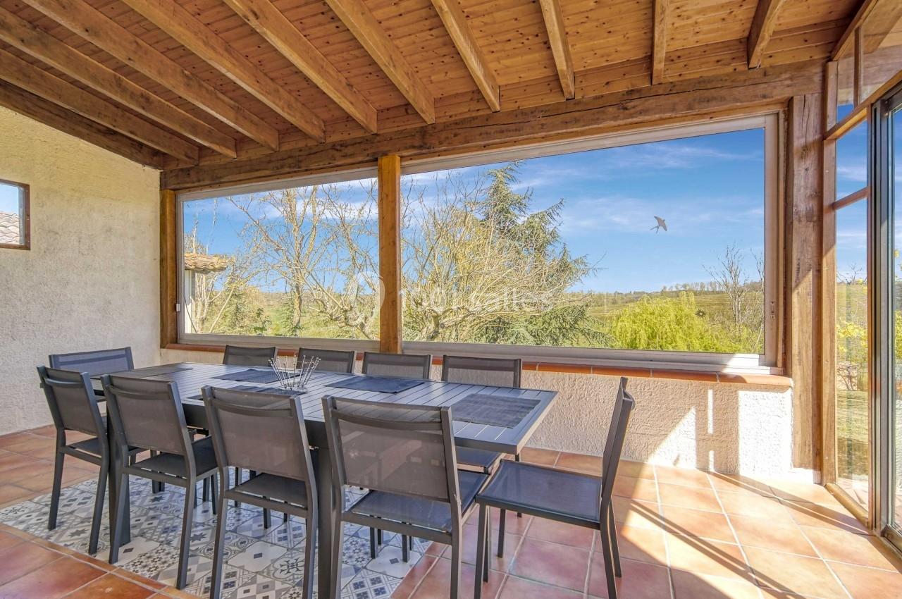 Salle à manger lumineuse avec une grande table entourée de chaises, vue dégagée sur un paysage arboré à travers de larges…