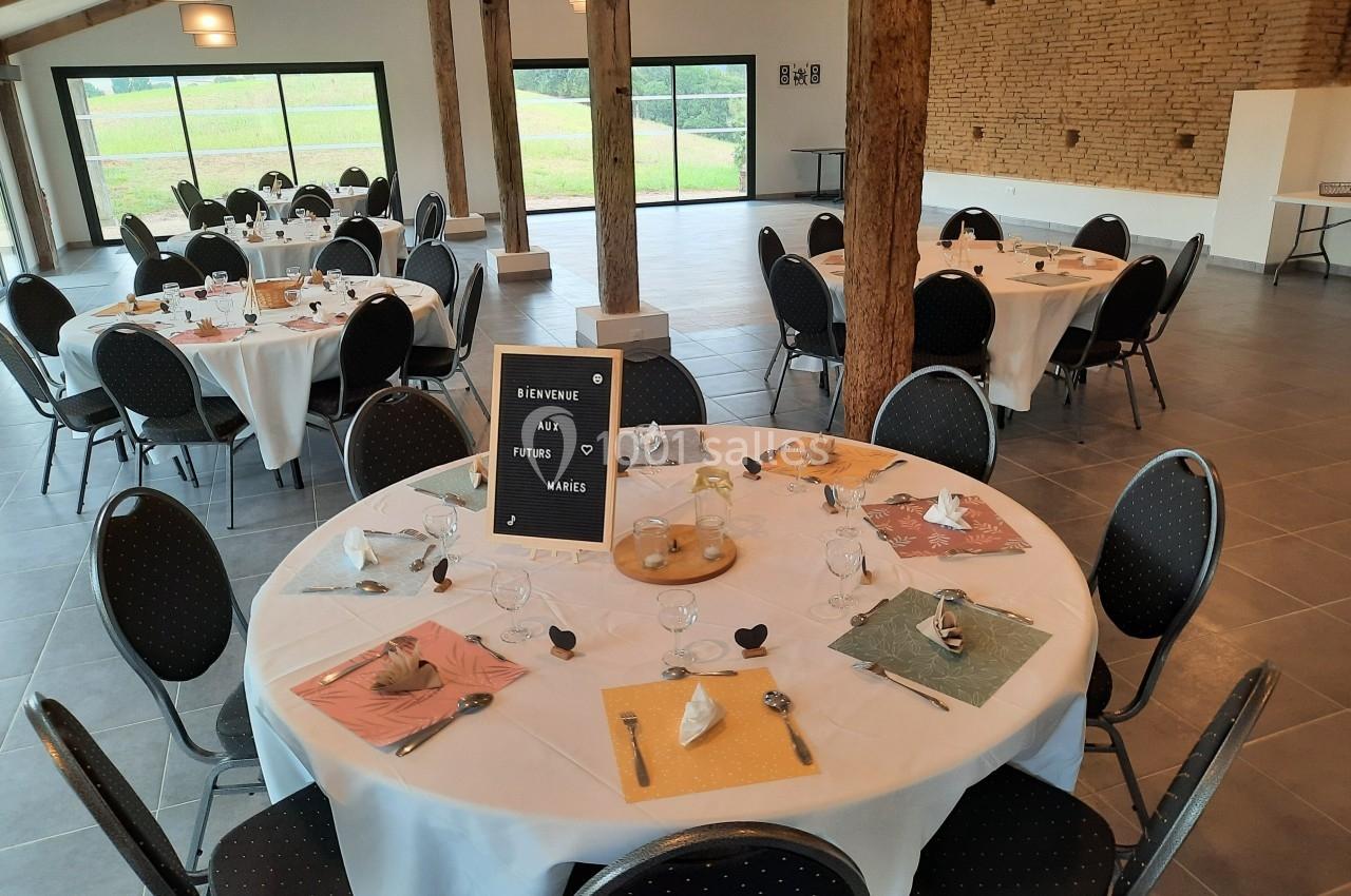 Salle de réception décorée avec des tables rondes dressées, vue sur l'extérieur à travers de grandes baies vitrées.