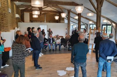 Un groupe de personnes participe à une réunion dans une salle avec des murs en pierre et une charpente apparente.