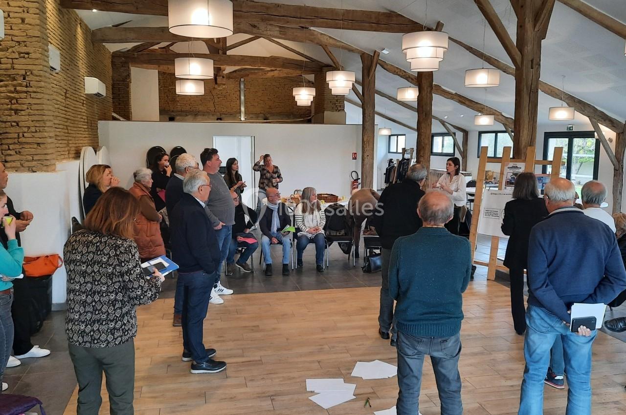 Un groupe de personnes participe à une réunion dans une salle avec des murs en pierre et une charpente apparente.