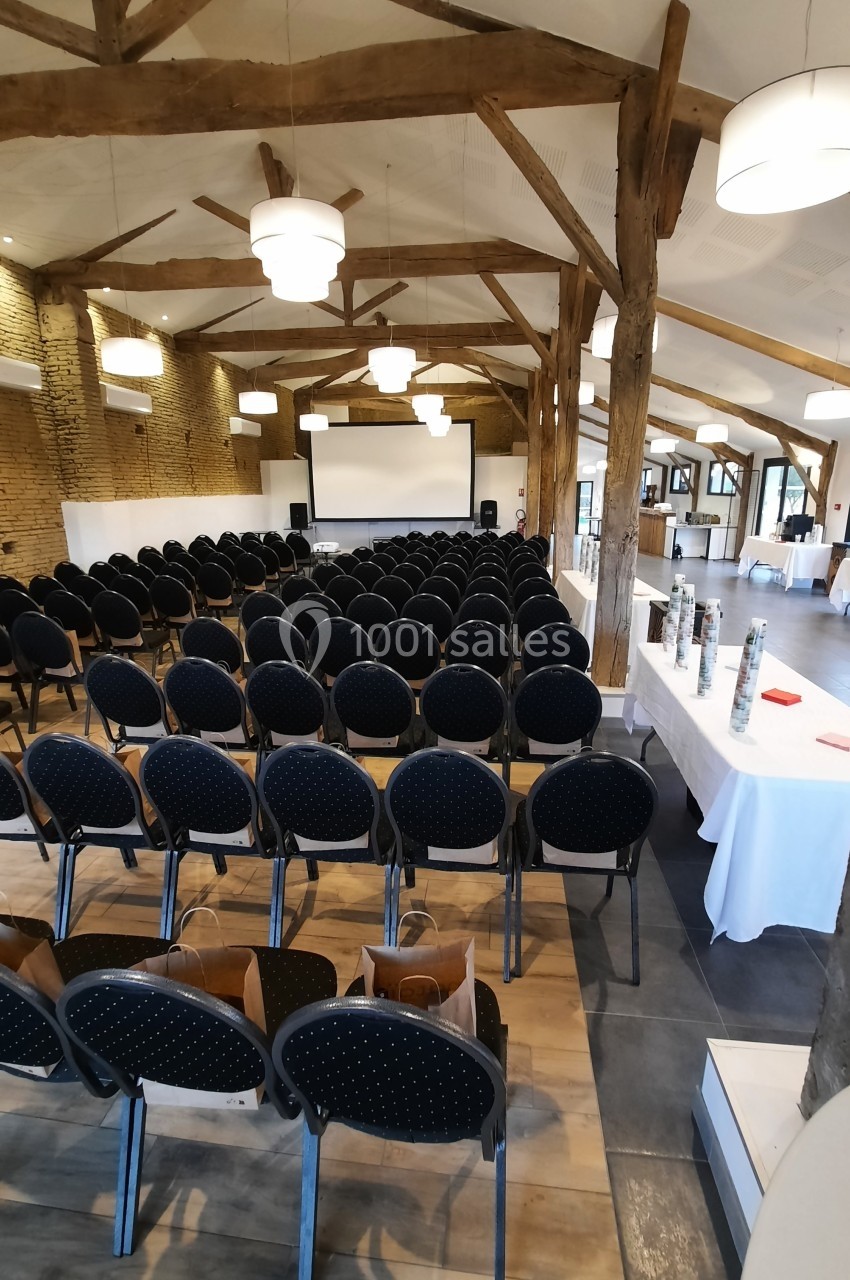 Salle de conférence avec rangées de chaises noires, écran de projection et tables dressées sur le côté.
