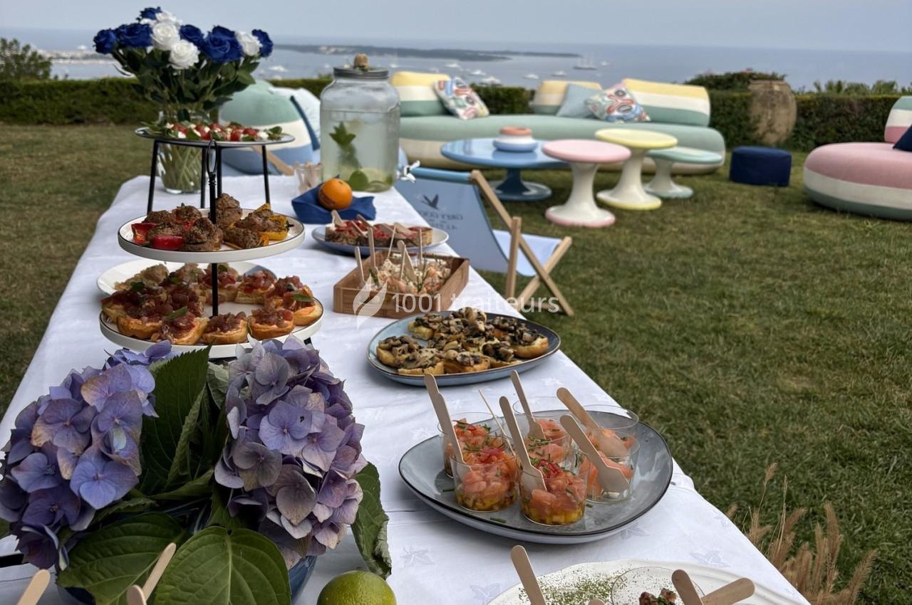 Buffet en plein air avec verrines, amuse-bouches et fleurs, installé sur une pelouse avec vue sur la mer.