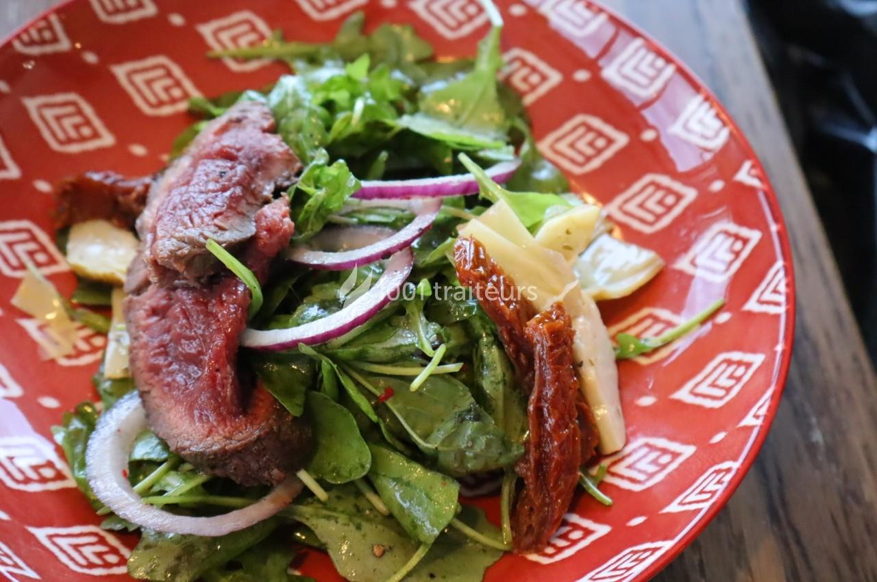 Salade composée avec roquette, tranches de bœuf, oignons rouges, tomates séchées et morceaux de fromage.