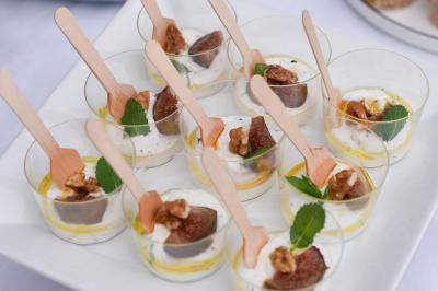 Verrines de fromage frais garnies de figues, noix, feuilles de menthe et cuillères en bois sur un plateau blanc.