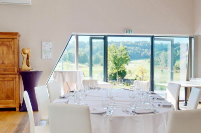 Miniature Location salle Pulnoy (Meurthe-et-Moselle) - Restaurant du Golf de Pulnoy #3 Salle de réception lumineuse avec des tables rondes dressées pour un événement, entourées de chaises blanches.