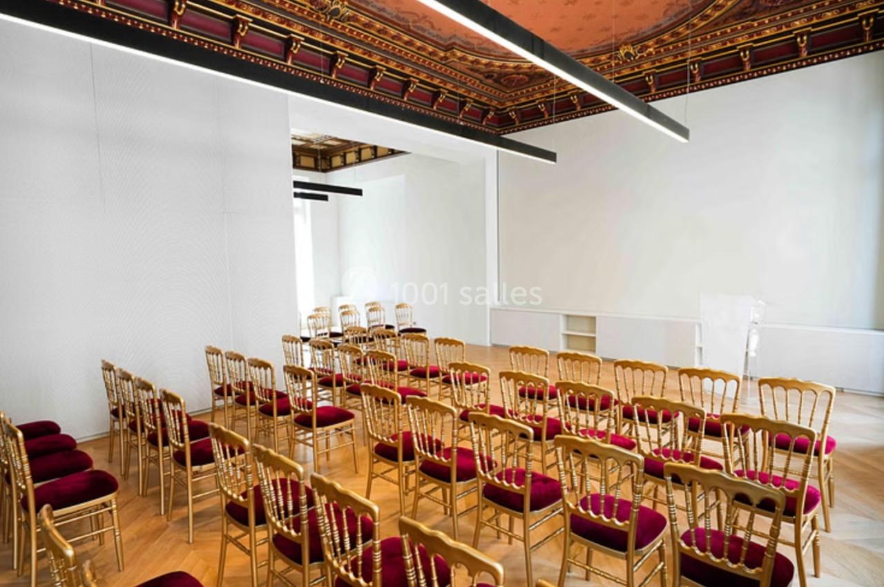 Salle lumineuse avec chaises dorées et coussins rouges, plafond décoratif et parquet en bois clair.