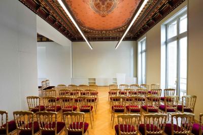 Un groupe de mannequins en tenues élégantes défile sur une scène, observé par un public dans une salle lumineuse.