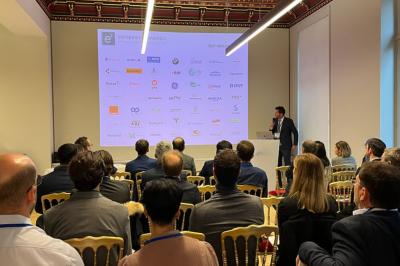 Un groupe de mannequins en tenues élégantes défile sur une scène, observé par un public dans une salle lumineuse.