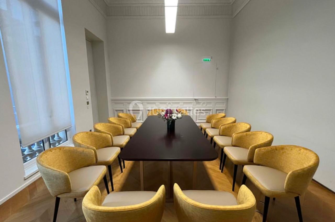 Salle de réunion avec une table rectangulaire sombre entourée de chaises jaunes et un vase de fleurs au centre.