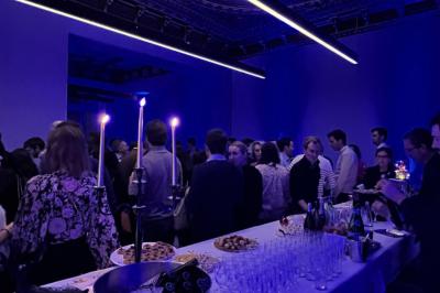 Un groupe de mannequins en tenues élégantes défile sur une scène, observé par un public dans une salle lumineuse.