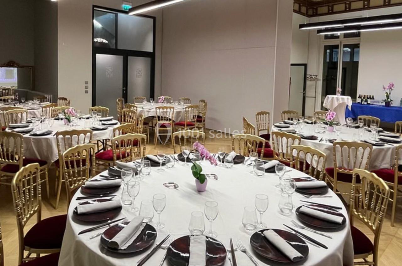 Salle de réception élégante avec tables rondes dressées, chaises dorées et buffet en arrière-plan.