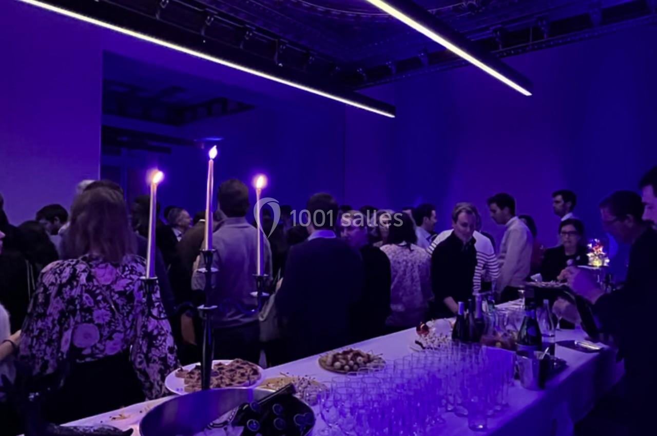 Un groupe de personnes échange dans une salle éclairée par une lumière violette, avec une table de buffet au premier plan.