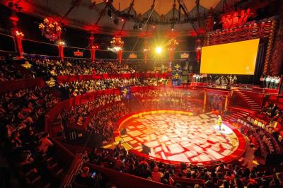 Salle vide avec éclairage rouge, rideaux en arrière-plan, scène surélevée et comptoirs alignés sur les côtés.