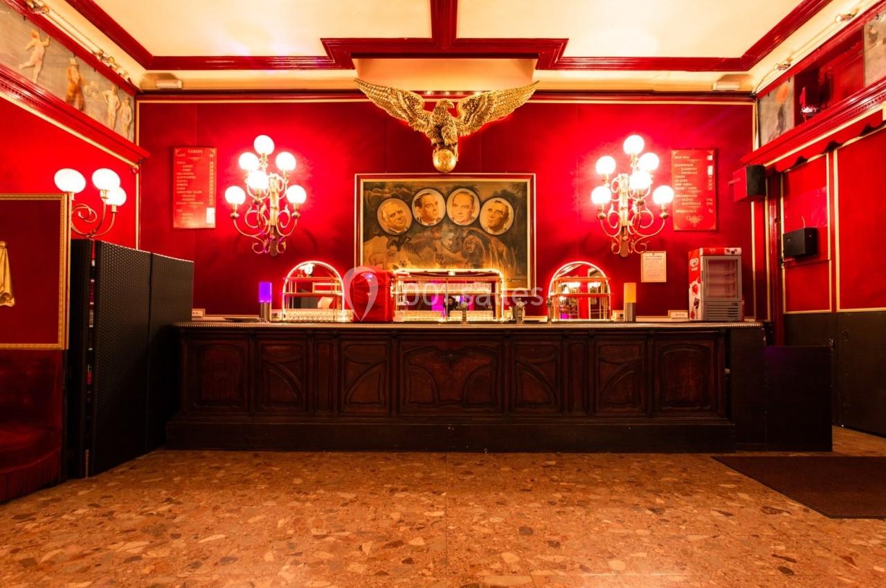 Comptoir en bois sombre dans un intérieur rouge avec lustres, tableau central et décoration dorée en forme d'aigle.