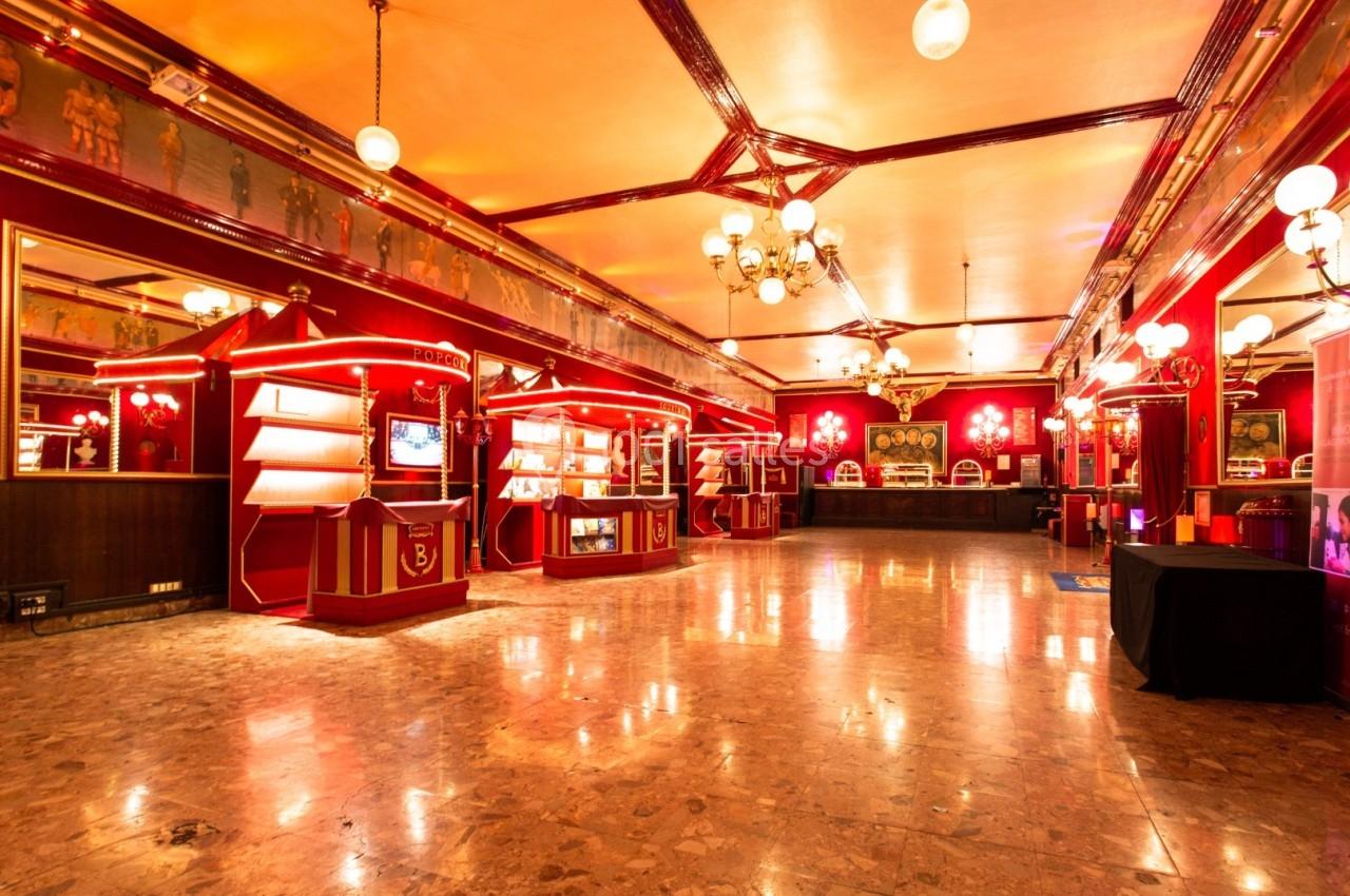 Salle spacieuse au décor rétro avec éclairage chaleureux, murs rouges, vitrines et lustres suspendus.