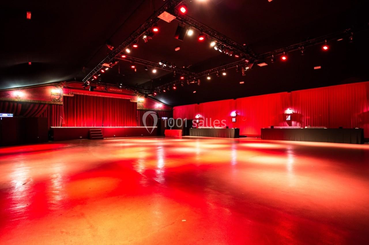 Salle vide avec éclairage rouge, rideaux en arrière-plan, scène surélevée et comptoirs alignés sur les côtés.