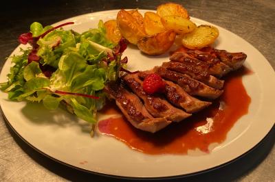 Assiette composée de magret de canard tranché avec sauce, pommes de terre rôties et salade verte.