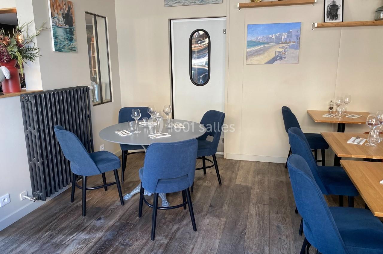 Salle de restaurant avec tables dressées, chaises bleues et décoration murale sobre dans un cadre lumineux.