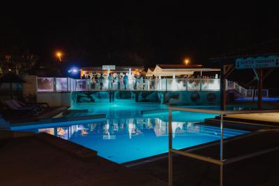 Terrasse en bois avec table dressée, chaises noires, barbecue et vue sur des toits de maisons, sous une pergola rouge.