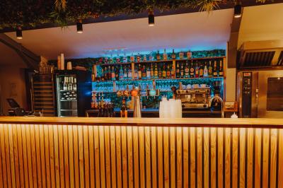 Terrasse en bois avec table dressée, chaises noires, barbecue et vue sur des toits de maisons, sous une pergola rouge.
