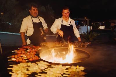 Terrasse en bois avec table dressée, chaises noires, barbecue et vue sur des toits de maisons, sous une pergola rouge.