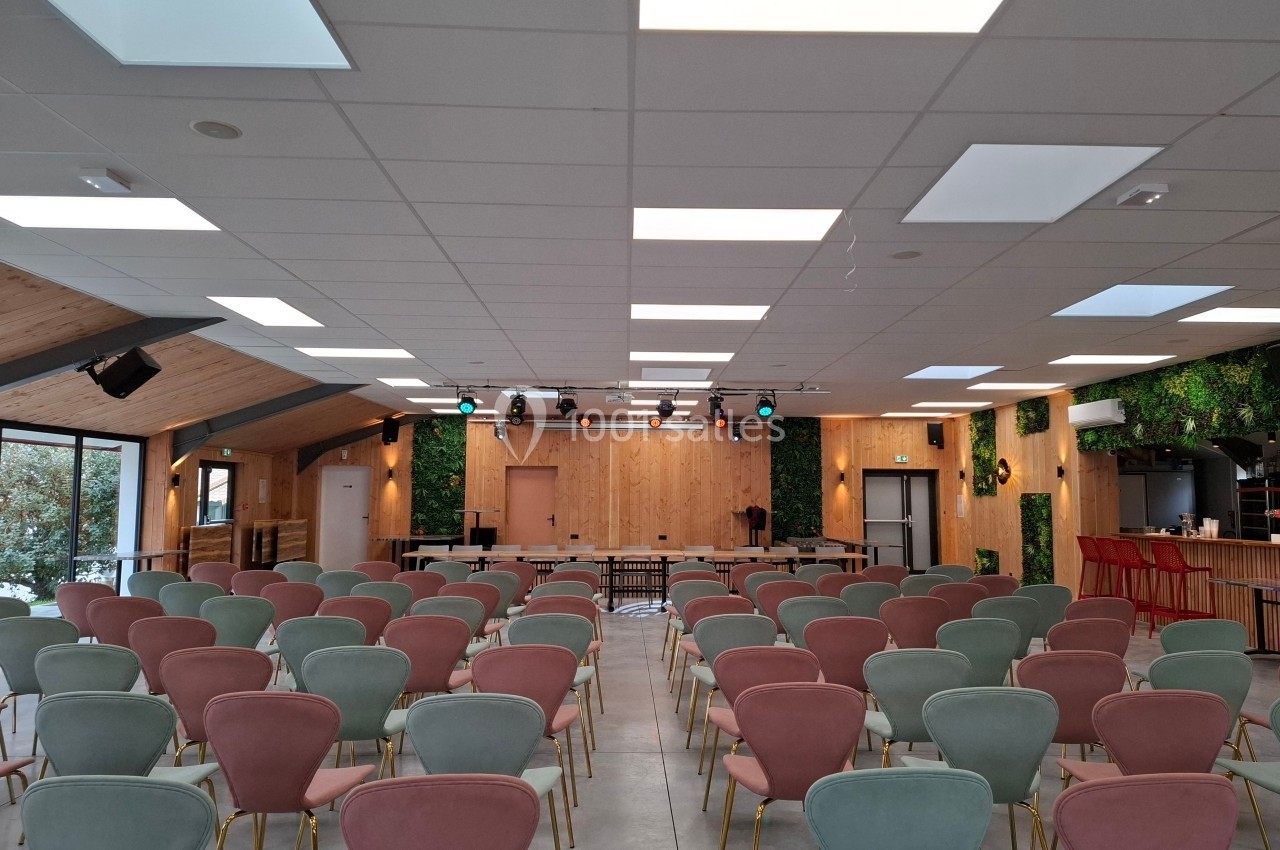 Salle de conférence lumineuse avec des rangées de chaises colorées, un plafond moderne et une scène en bois.