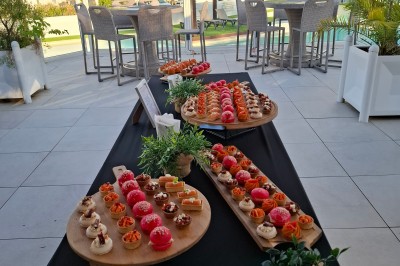 Plateau de bouchées apéritives variées disposé sur une table noire en terrasse avec vue sur un espace extérieur verdoyant.