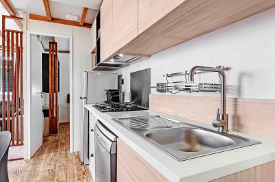 Terrasse en bois avec table dressée, chaises noires, barbecue et vue sur des toits de maisons, sous une pergola rouge.