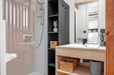 Terrasse en bois avec table dressée, chaises noires, barbecue et vue sur des toits de maisons, sous une pergola rouge.