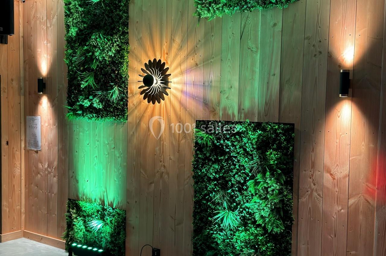 Mur en bois décoré de panneaux végétaux éclairés par des spots verts et des appliques murales.