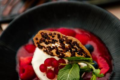 Terrasse en bois avec table dressée, chaises noires, barbecue et vue sur des toits de maisons, sous une pergola rouge.