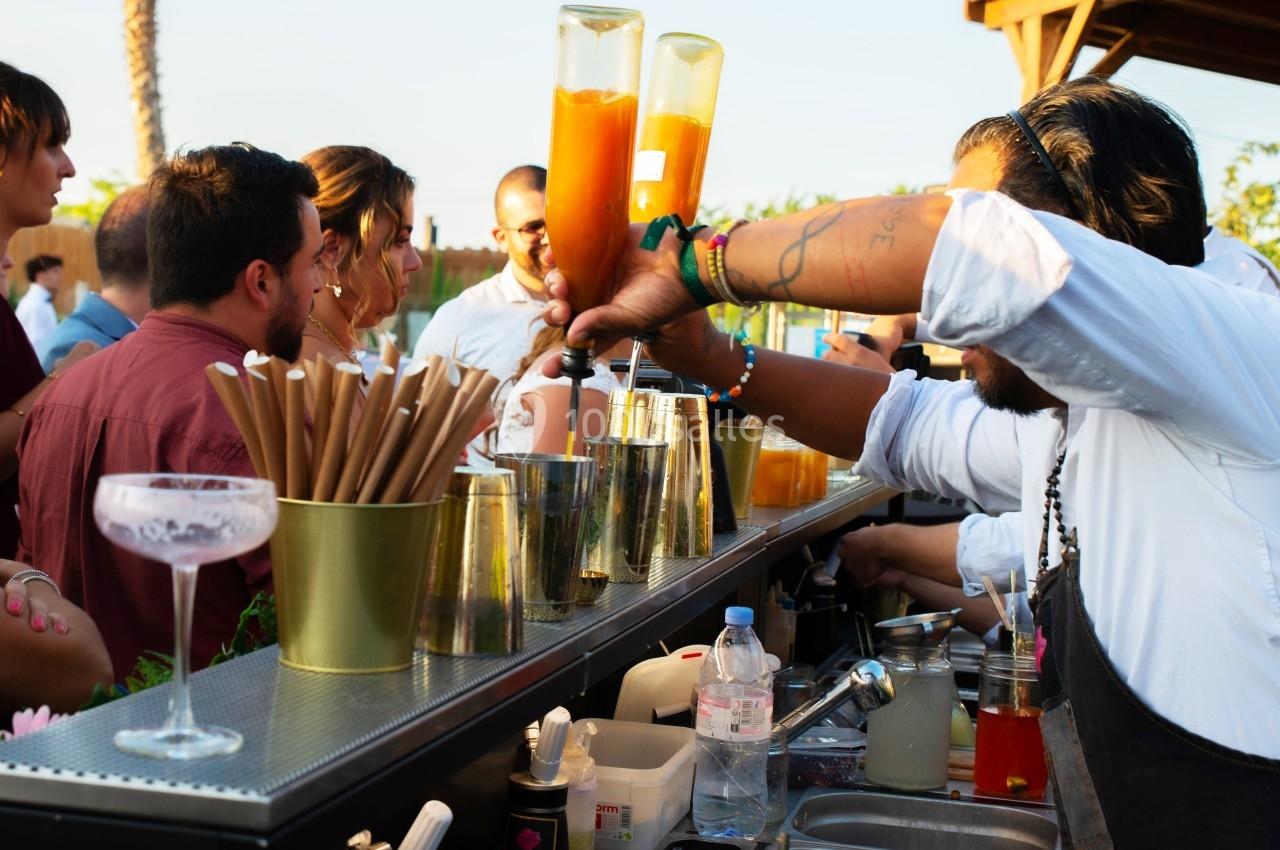 Un barman prépare des cocktails devant un groupe de personnes lors d'un événement en plein air.