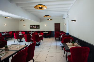 Terrasse en bois avec table dressée, chaises noires, barbecue et vue sur des toits de maisons, sous une pergola rouge.