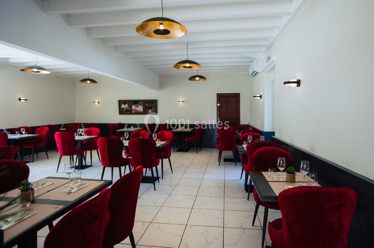 Salle de restaurant lumineuse avec des chaises rouges, des tables dressées et des suspensions dorées au plafond.
