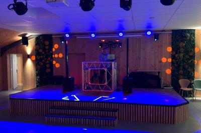 Terrasse en bois avec table dressée, chaises noires, barbecue et vue sur des toits de maisons, sous une pergola rouge.