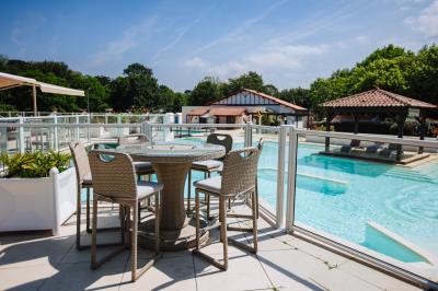 Terrasse en bois avec table dressée, chaises noires, barbecue et vue sur des toits de maisons, sous une pergola rouge.